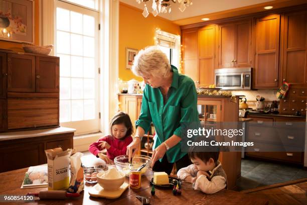 grandmother with kids preparing cookies at home during christmas - butter making fotografías e imágenes de stock