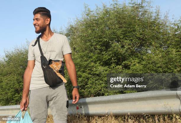 An Afghan man carries his cat Rocky outside in a bag after retrieving NGO-provided food outside the Moria refugee camp on May 20, 2018 in Mytilene,...