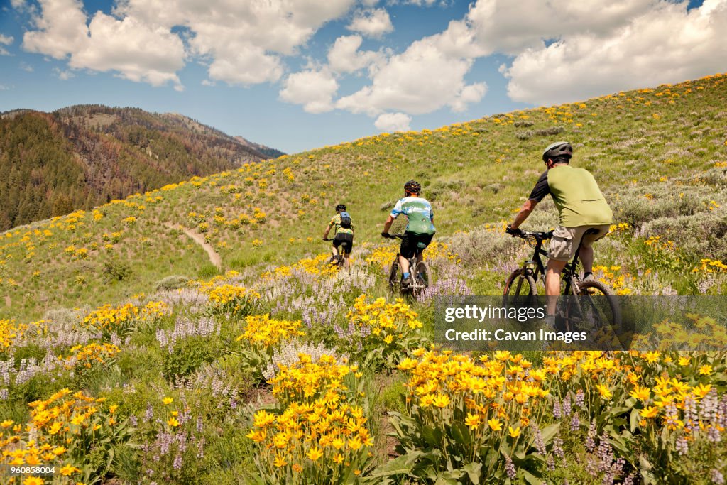 Friends riding bicycle on hill against cloudy sky
