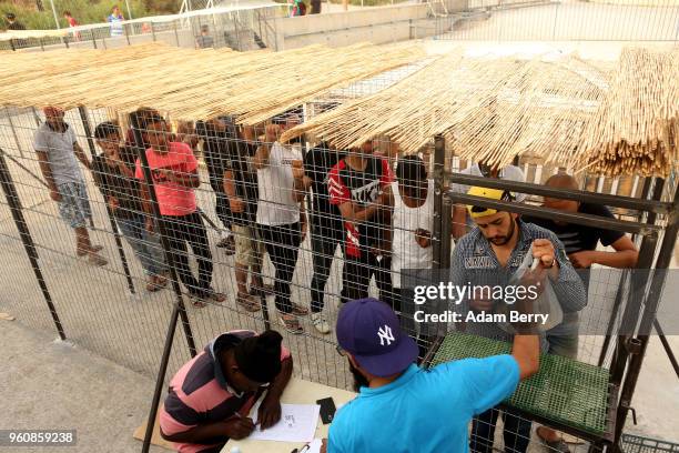 Refugees wait in line for bags of hot beans and rice at an independent, NGO-run food distribution center outside the Moria refugee camp on May 20,...