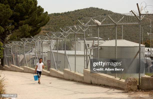 Refugee carries a bucket to fill with water at the Moria refugee camp on May 20, 2018 in Mytilene, Greece. Despite being built to hold only 2,500...