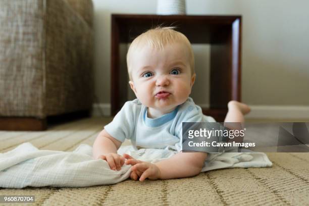 portrait of cute playful baby boy making face while lying on carpet at home - making a face stock-fotos und bilder