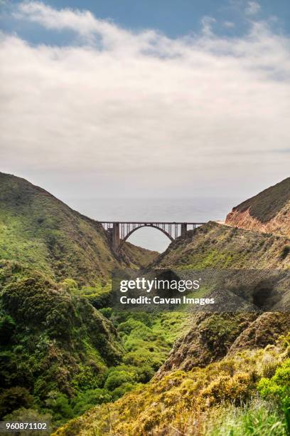 scenic view of bixby creek bridge amidst mountains against cloudy sky - ビクスビークリーク ストックフォトと画像