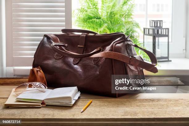 leather bag and books on table at home office by window - sac en cuir photos et images de collection