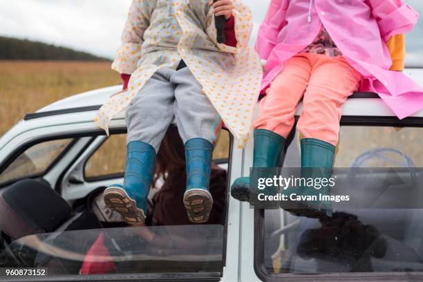 low section of siblings sitting on car roof - russia rain boots imagens e fotografias de stock