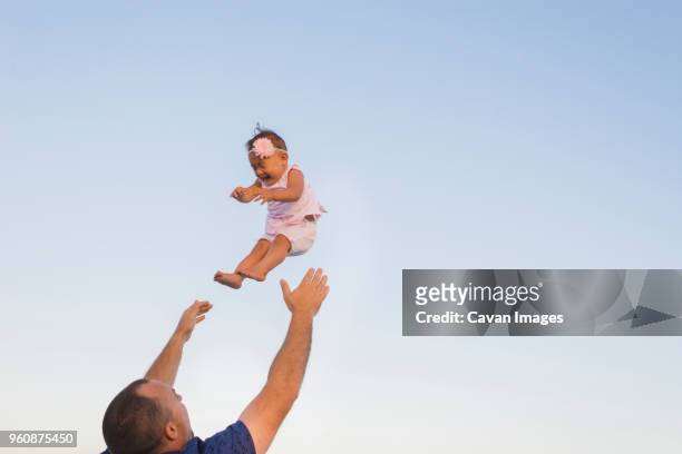 low angle view of father throwing daughter into air against clear sky - dad throwing kid in air stockfoto's en -beelden
