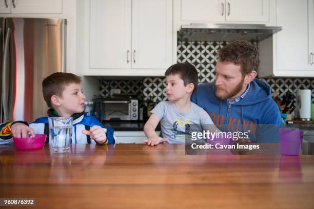 father and sons eating snacks on table at home - genderblend2015 stock pictures, royalty-free photos & images