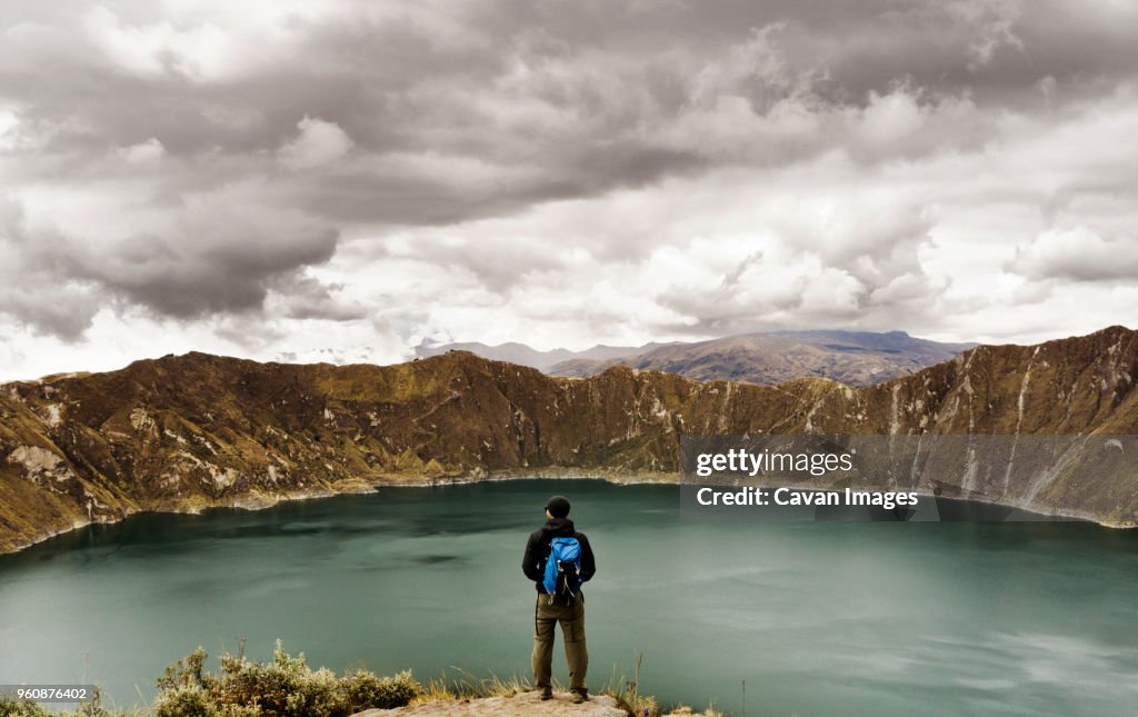 Rear view of man standing on cliff against Quilotoa and cloudy sky