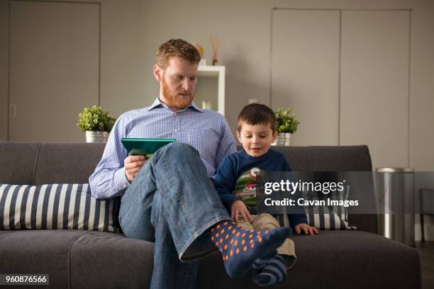 father and son sitting on sofa at home - genderblend2015 stock pictures, royalty-free photos & images