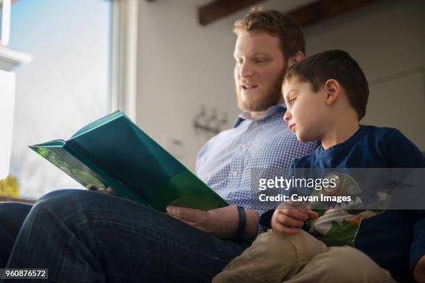 low angle view of father and son looking at book - genderblend2015 stock pictures, royalty-free photos & images