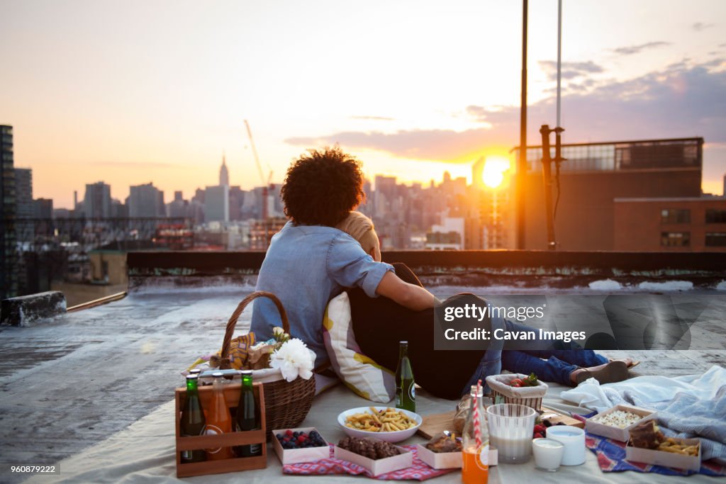 Couple relaxing on rooftop against sky during picnic