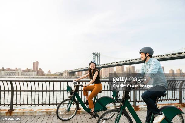 happy couple cycling on footpath by manhattan bridge against sky - city breaks stock pictures, royalty-free photos & images