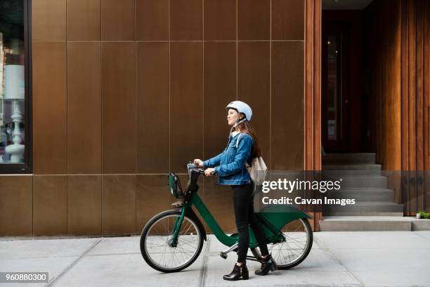 woman walking with bicycle on sidewalk by building - cavan images stock pictures, royalty-free photos & images
