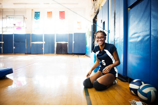 portrait of smiling teenage girl sitting on floor in volleyball court - girls volleyball stock pictures, royalty-free photos & images