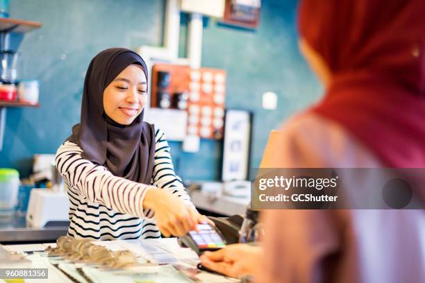 reaching out to hand the credit card over - malaysian people stock pictures, royalty-free photos & images