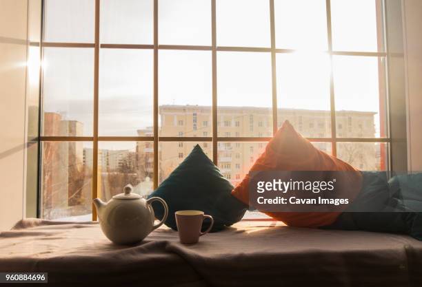kettle with cup by cushions on alcove window seat at home - window seat fotografías e imágenes de stock