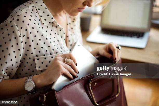 midsection of woman putting tablet computer in purse at home office - handtasche stock-fotos und bilder