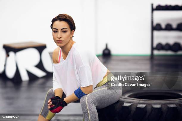 portrait of confident female athlete sitting on tire at gym - gloves clasped hands ストックフォトと画像