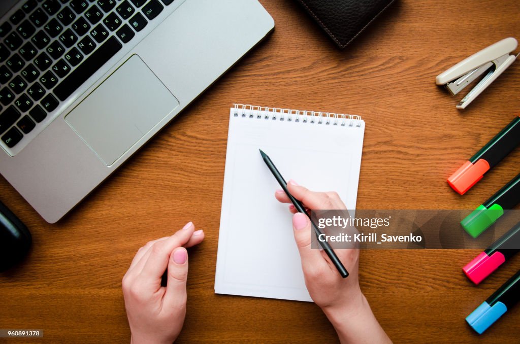 White notepad hand girl writing on a wooden table texture background. Laptop and phone for work. Concept art, design, success, idea, start-up, at work, education