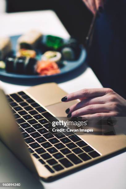 cropped hand on businesswoman using laptop computer while having food at desk in home office - touchpad stock-fotos und bilder