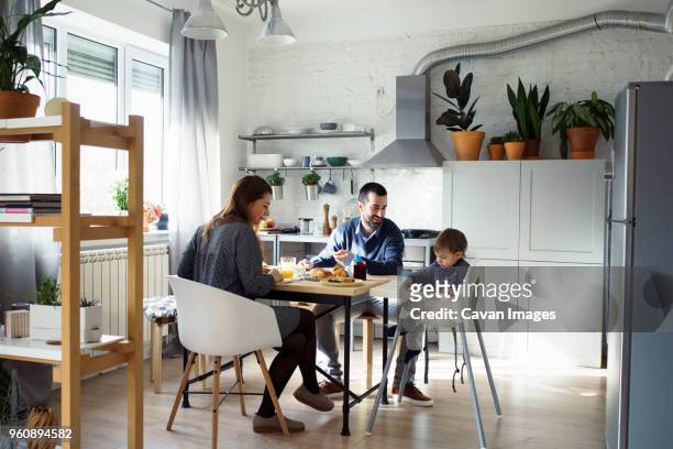 parents looking at son sitting on high chair while having breakfast in kitchen - refrigerator front stock pictures, royalty-free photos & images