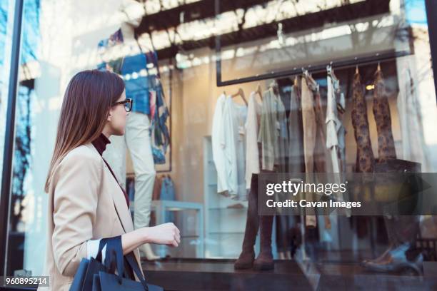 side view of woman looking in shop window while shopping in city - etalages kijken stockfoto's en -beelden