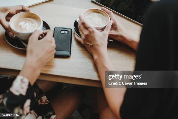 midsection of friends holding cappuccino on table while sitting at cafe - cup saucer stock pictures, royalty-free photos & images