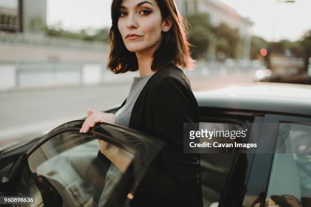 portrait of confident woman boarding into car in city - entrando fotografías e imágenes de stock