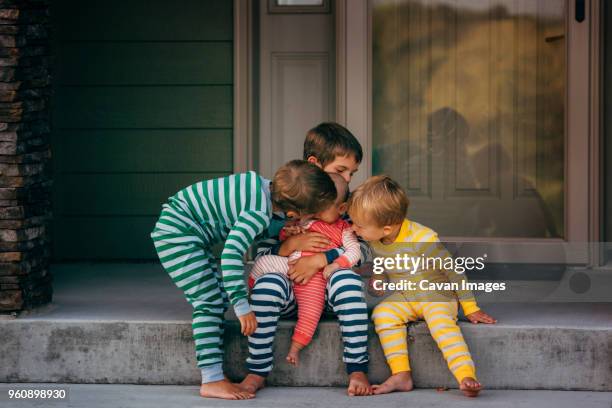 loving brothers kissing sister in front of house - family of four in front of house stock pictures, royalty-free photos & images