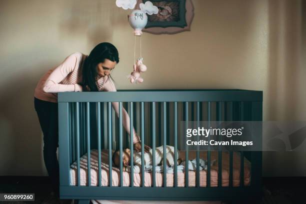 mother looking at daughter sleeping in crib at home - baby cot stock pictures, royalty-free photos & images