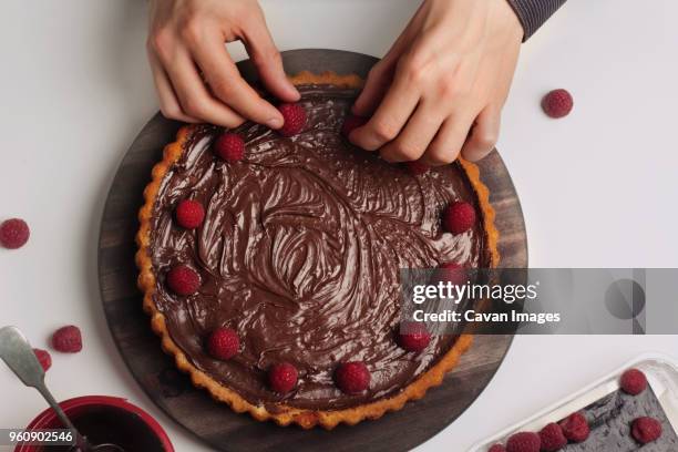 man decorating chocolate tart with raspberries - raised finger stock-fotos und bilder