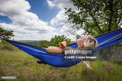 Woman holding apple while lying on hammock at field during vacation Woman holding apple while lying on hammock at field during vacation