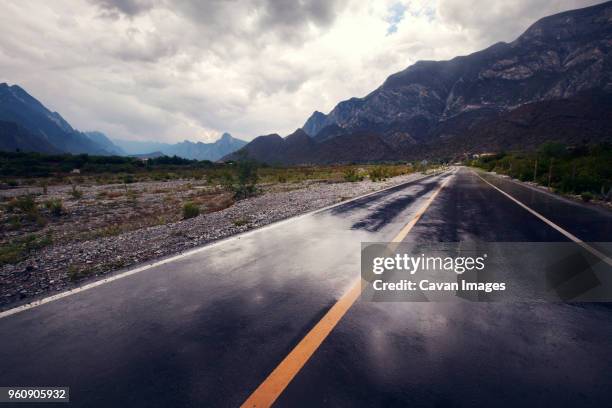 empty road leading towards mountains against cloudy sky - monterrey stockfoto's en -beelden