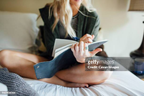 low section of woman writing diary while sitting on bed - diary photos et images de collection
