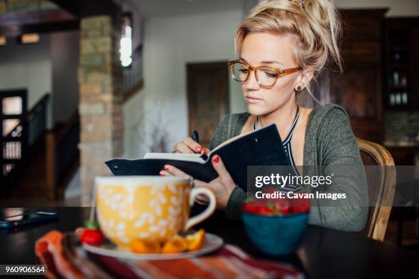 woman writing diary while sitting at breakfast table - meal planning stock pictures, royalty-free photos & images