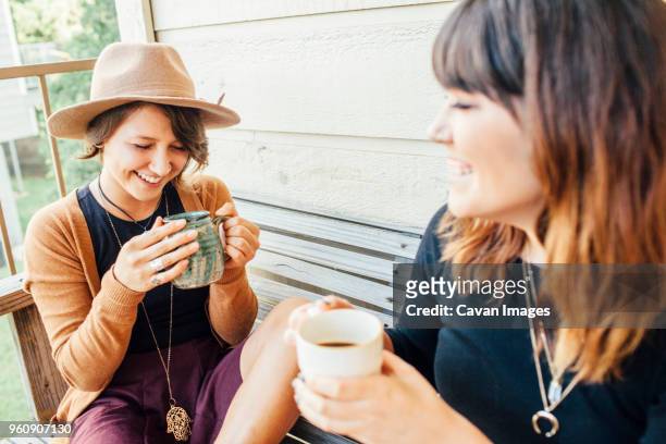 smiling female friends having coffee while sitting on wooden bench - cavan images stockfoto's en -beelden