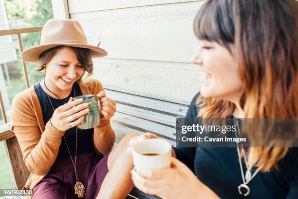 smiling female friends having coffee while sitting on wooden bench - cavan images stock pictures, royalty-free photos & images