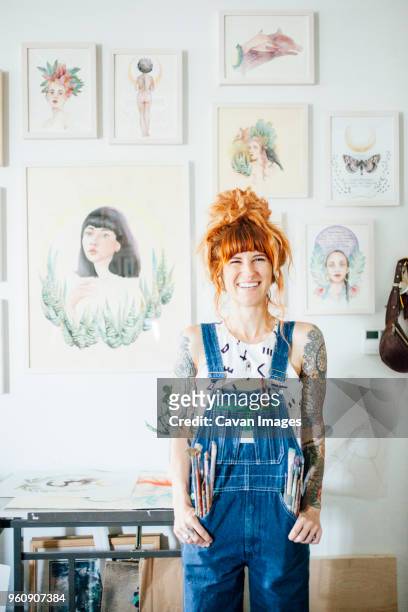 portrait of smiling artist with hands in pockets standing in studio - pittore artista foto e immagini stock