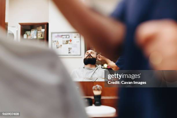 midsection of barber cutting man beard reflecting on mirror at salon - italienischer abstammung stock-fotos und bilder