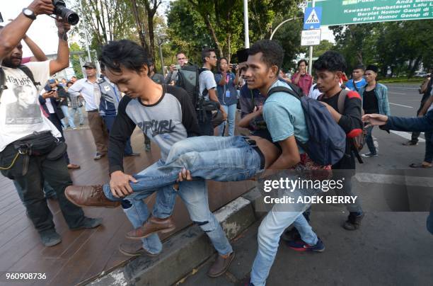 Indonesian students carry an injured student after a brief clash with policemen outside the presidential palace during a rally to mark the 20th years...