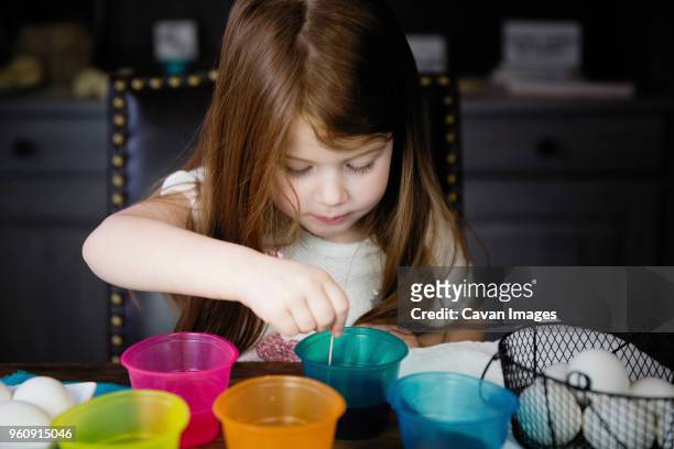 cute girl coloring easter eggs on table at home - dip dye stock pictures, royalty-free photos & images