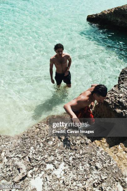 high angle view of man looking at friend moving up rocky steps - aruba beach stock-fotos und bilder