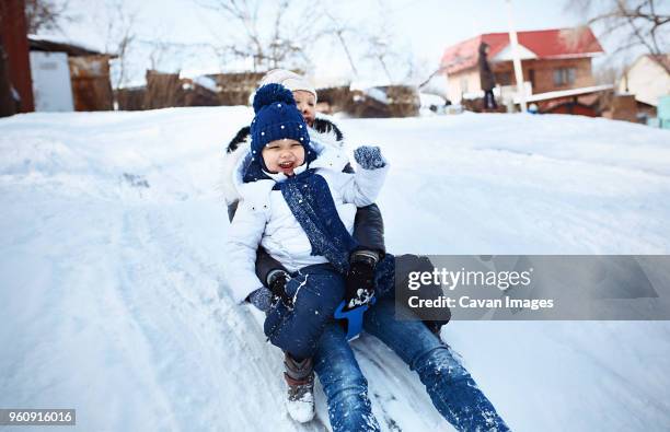 cheerful mother and daughter tobogganing on snowy field - family sports centre laughing stock pictures, royalty-free photos & images