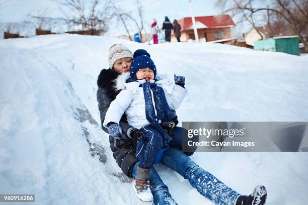 mother and daughter tobogganing on snowy field - asian family fall stock-fotos und bilder