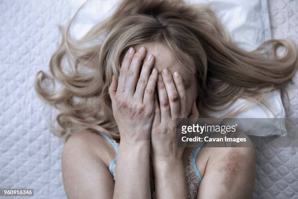 woman covering face with hands while lying on bed at home - violence foto e immagini stock