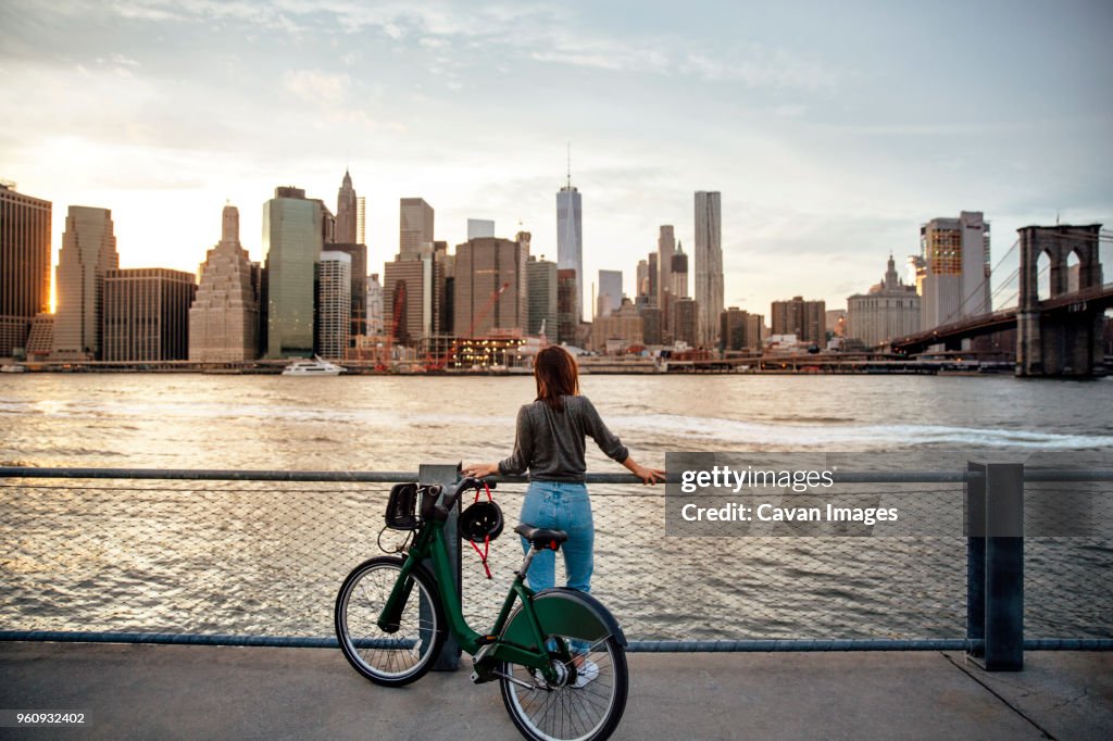 Rear view of woman with bicycle looking at city view while standing on observation point