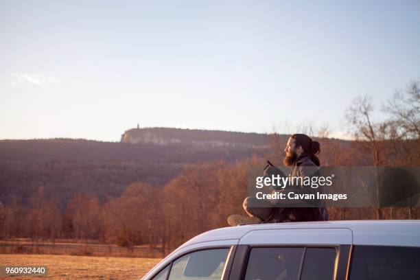 side view of man sitting with dog on car roof against clear sky - car roof stock pictures, royalty-free photos & images