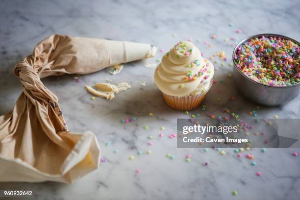 high angle view of icing bag by cupcake and sprinkles on kitchen counter - cupcake stock pictures, royalty-free photos & images