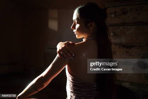 rear view of woman applying oil to body in darkroom at home - aromatherapy oil stock pictures, royalty-free photos & images