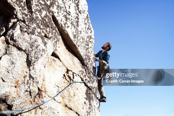 low angle view of man rock climbing against clear sky - rock face stock pictures, royalty-free photos & images